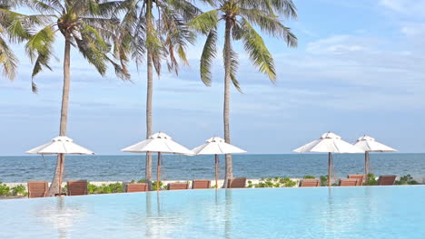 infinity pool lounge with set up deckchairs and umbrellas in seafront beach at exotic ilsand in thailand on cloudy day