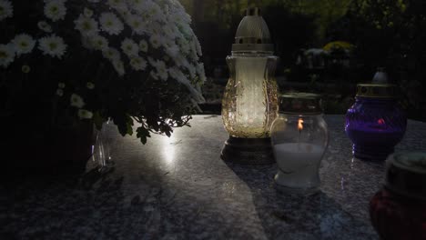 a grave illuminated from behind as a hand places a candle on it, symbolizing reverence and remembrance in a solemn moment