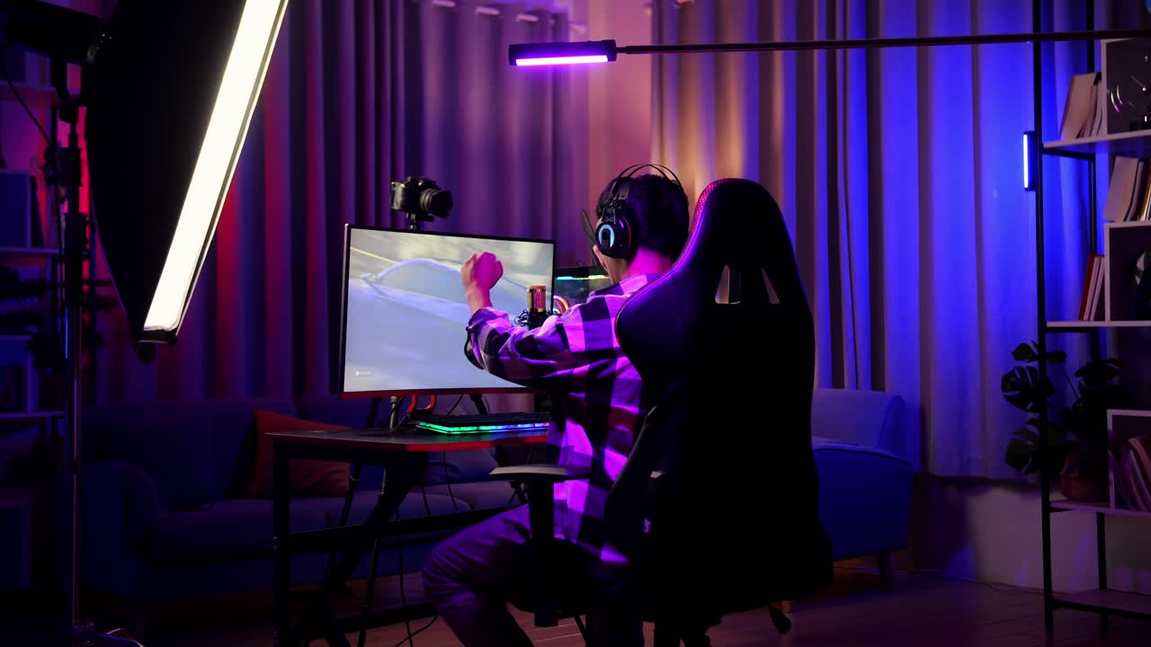vista trasera de streamer chico asiático gritando gol y bailando celebrando ganando juego de carreras de coches a través de la red en computadora personal. videojuego de transmisión en vivo, escritorio iluminado por rgb led strip light