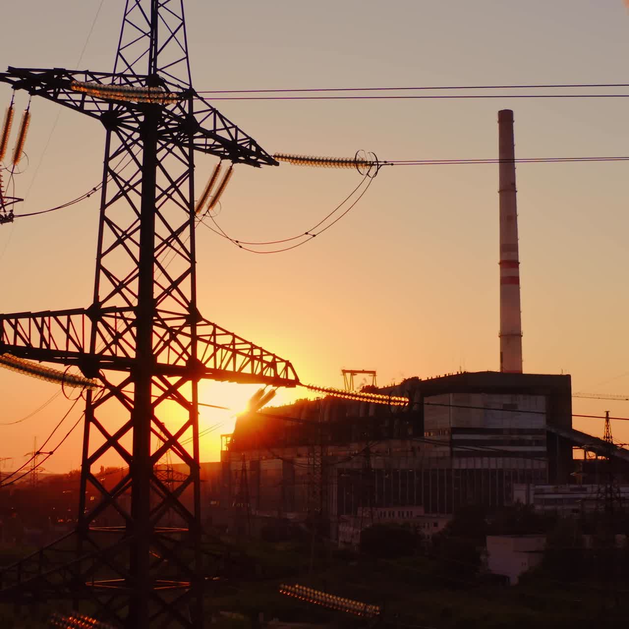 Industrial high voltage electricity tower. Silhouette of high voltage electric tower on sunset time. Industrial factory against the evening sky on sunset time background.