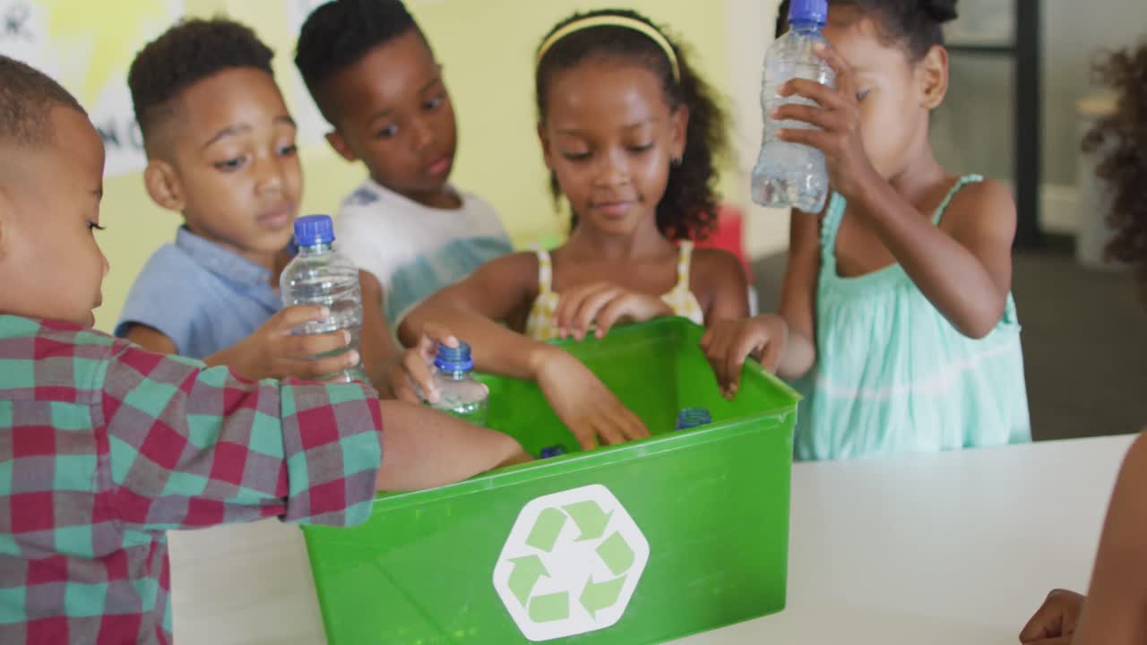 video de alumnos afroamericanos felices clasificando botellas de plástico para reciclar en el aula