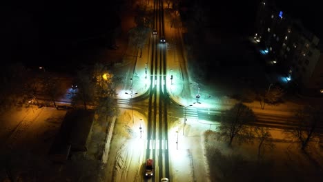vista aérea de la ciudad de liepaja durante la noche, paisaje urbano invernal, luces cálidas de la ciudad, intersección iluminada con camiones en movimiento, tiro amplio de drones, cámara inclinada hacia abajo