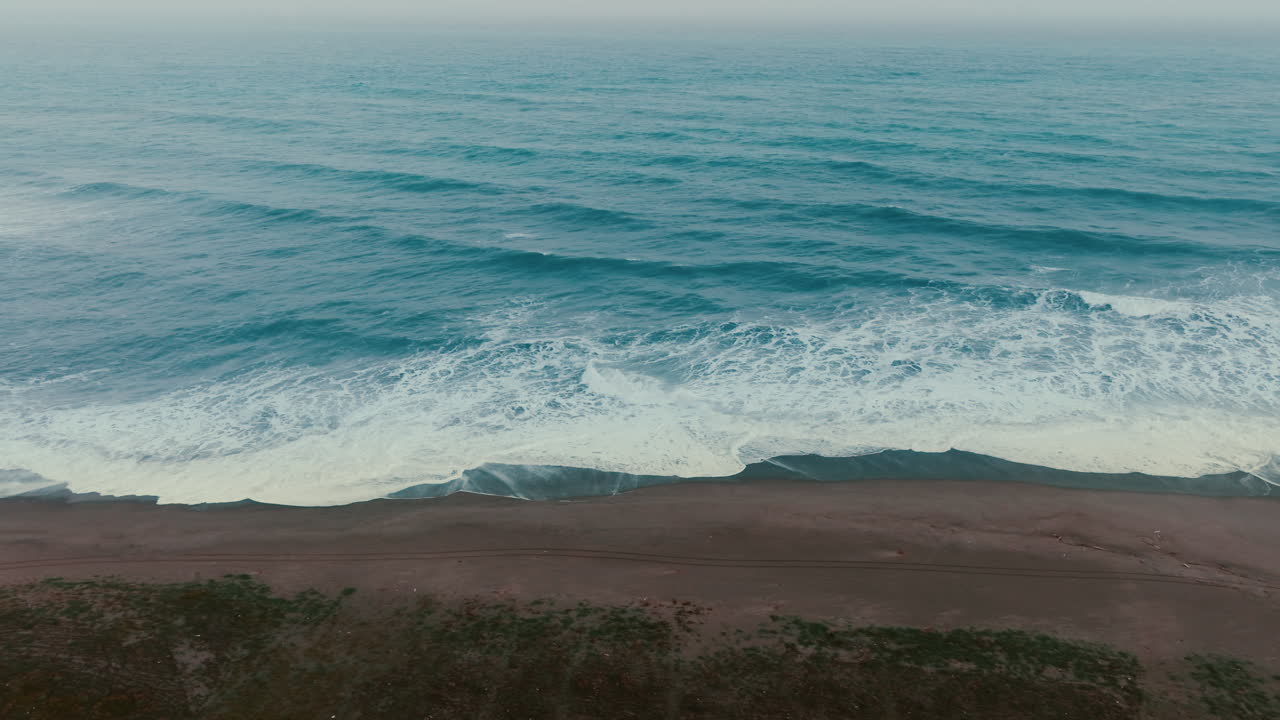 Onde oceaniche lunghe e ripetitive su spiaggia sabbiosa la sera, vista aerea