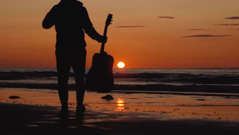 man running with guitar in back sand beach at sunset