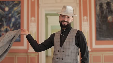 un hombre con sombrero y chaleco, sonriendo a la cámara en una galería de arte.