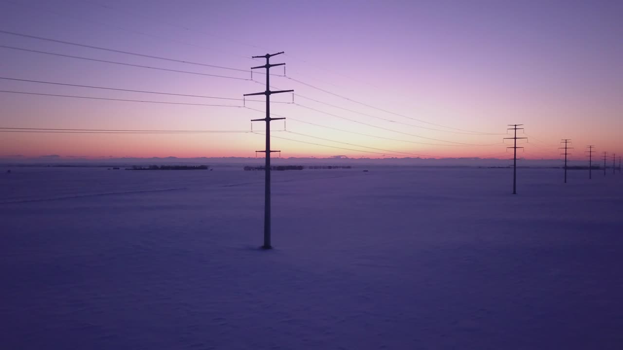Retreating aerial: Snow field power lines and colorful mountain sunset