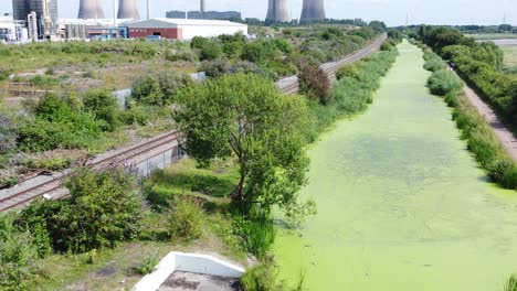 Green-algae-covered-canal-waterway-leading-to-power-station-industry-aerial-drone-view-slow-forward-tilt-up