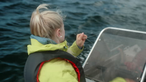 close-up of a pretty girl fishing on a small motor boat on a beautiful fjord in southern norway, amateur fishing, girl hauling back the fishing line