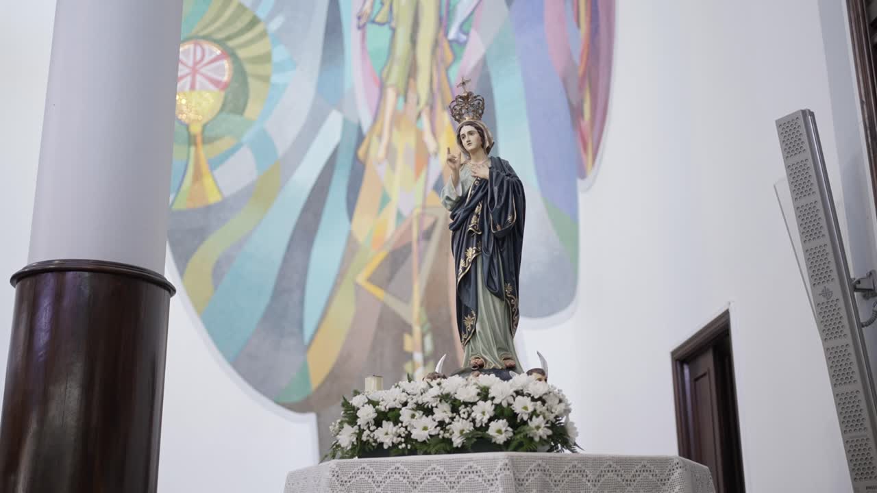 Sacred statue of Virgin Mary crowned with flowers and colorful mural background