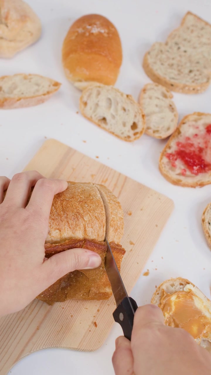 Close-up overhead shot of hands cutting crusty bread on a board with bright lighting.