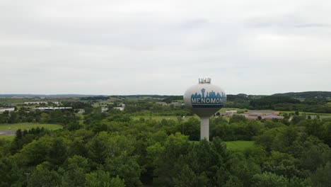 Antena-Giratoria-De-La-Torre-De-Agua-Que-Sostiene-El-Tanque-De-Agua,-De-Pie-Aislada-Y-Alta-En-Una-Exuberante-Vegetación-En-Menominee,-Wisconsin,-Estados-Unidos