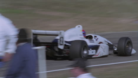 a race car drives around a track as people watch on the sidelines