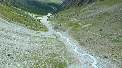 Vuelo-De-Drones-Sobre-Un-Sinuoso-Río-Glaciar-A-Través-De-Un-Valle-Alpino-De-Alta-Montaña