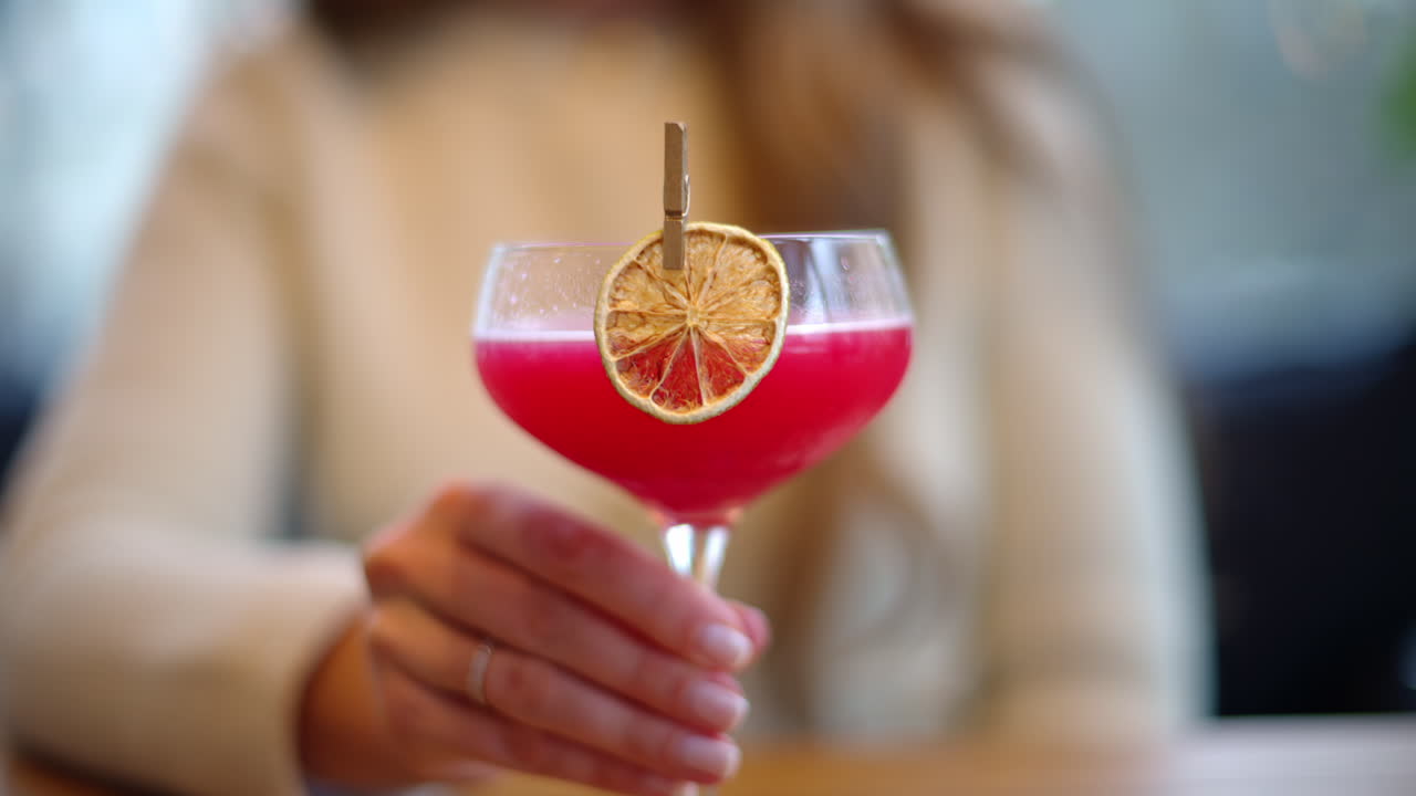 Donna che beve un cocktail rosso con arancia essiccata come decorazione