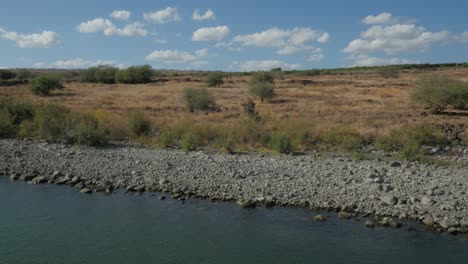 aerial, rocky lake shoreline with sparse brown vegetation on sunny day