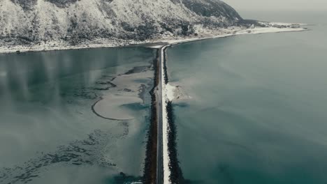 road between the body of water with snowy mountains in the distance. - aerial shot
