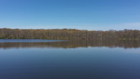 an aerial view of a blue, reflective lake with bare trees lining the lake's edge