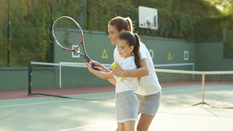 Liebevolle-Frau,-Die-Ihrer-Süßen-Kleinen-Tochter-Beibringt,-Wie-Man-An-Einem-Sommertag-Auf-Dem-Sportplatz-Tennis-Spielt