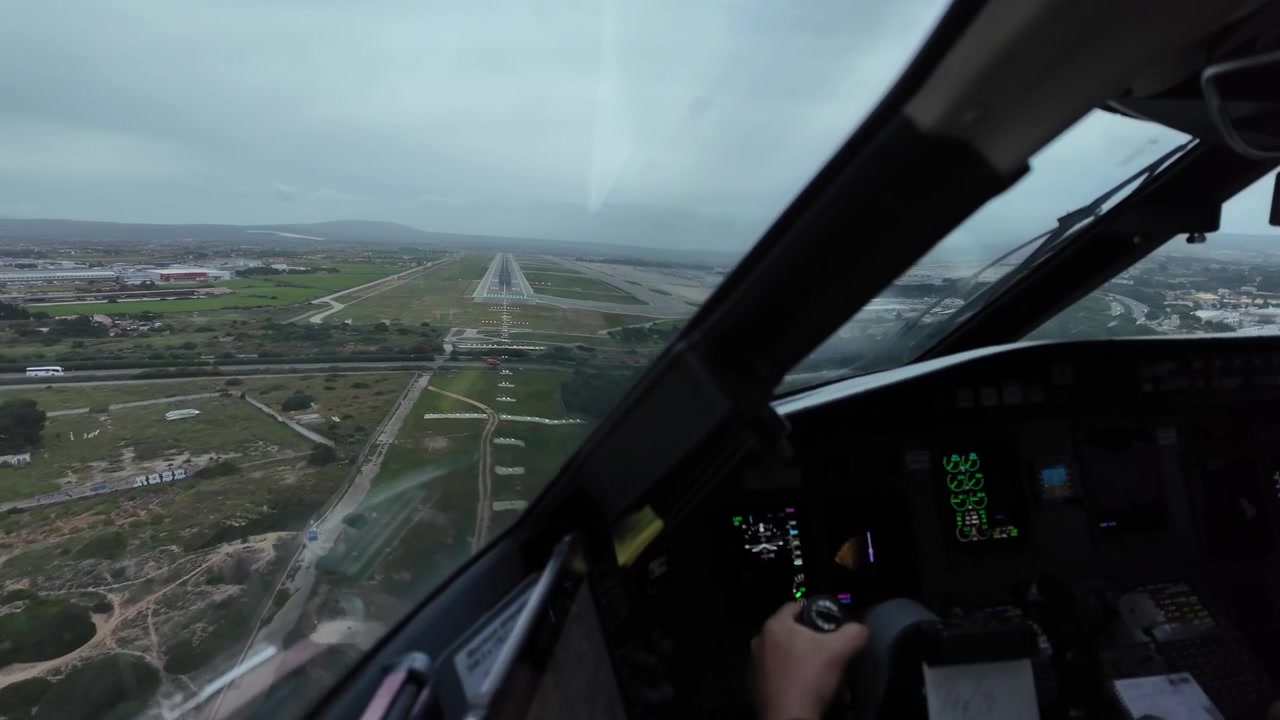 Immersive pilot’s eye view through the cockpit window of a jet airplane flying the final approach to Palma de Mallorca airport in a rainy and windy day, with a view of the pilot hand on the controls.