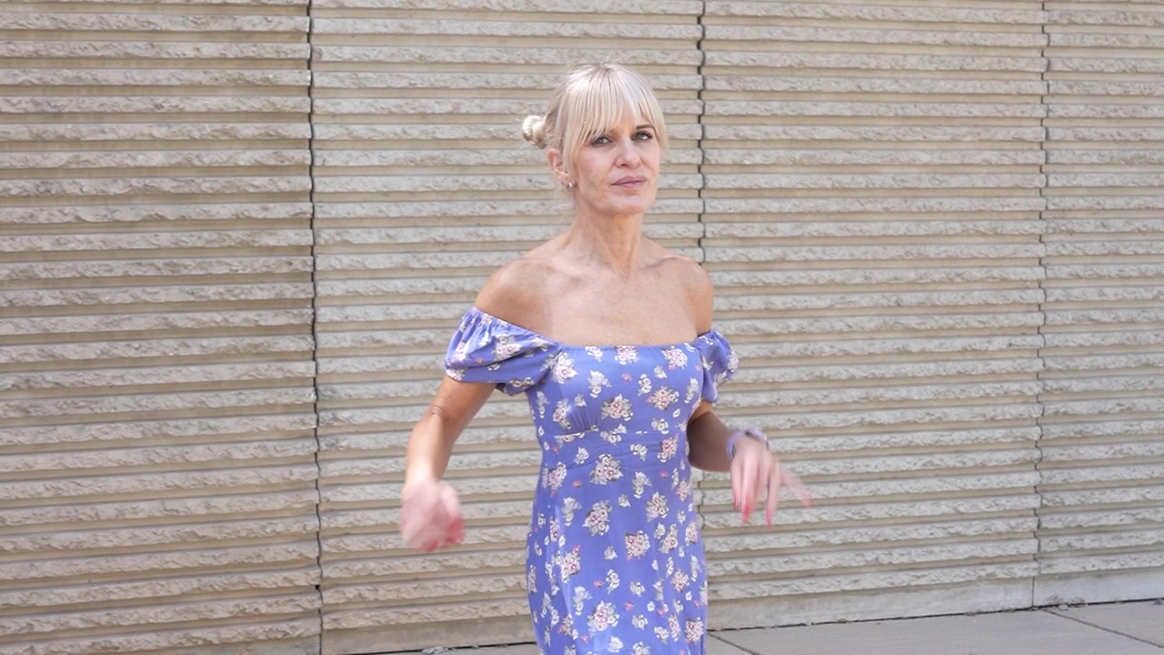 Una donna passeggia elegantemente all'aperto con un vestito floreale, irradiando fiducia e bellezza alla luce del sole.