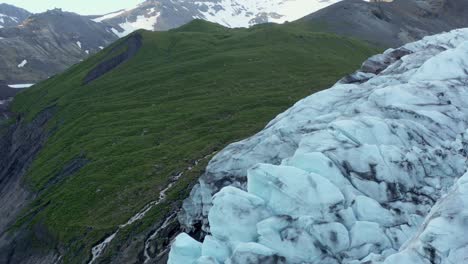 Green-grass-mountain-next-to-jagged-Falljökull-glacier-in-Iceland,-aerial