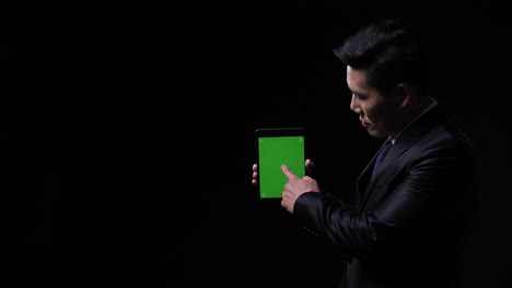 hombre de negocios asiático posando y mirando a la cámara con datos de presentación tableta pantalla verde. hombre trabajando sistema de inversión, billetera digital y servicio de diagnóstico. pantalla verde o llave de croma.