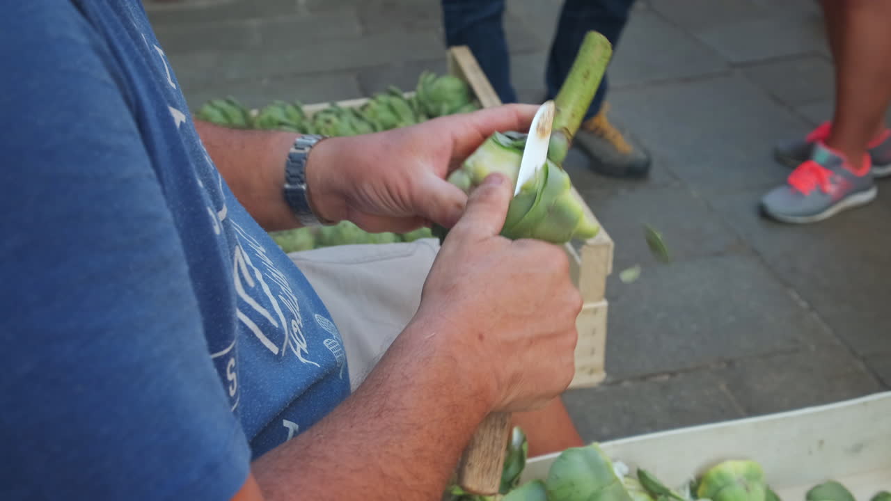 Close up slowmo of adult man cutting skin of artichoke with knife on road at food market in Venice