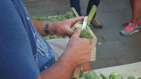 close up slowmo of adult man cutting skin of artichoke with knife on road at food market in venice