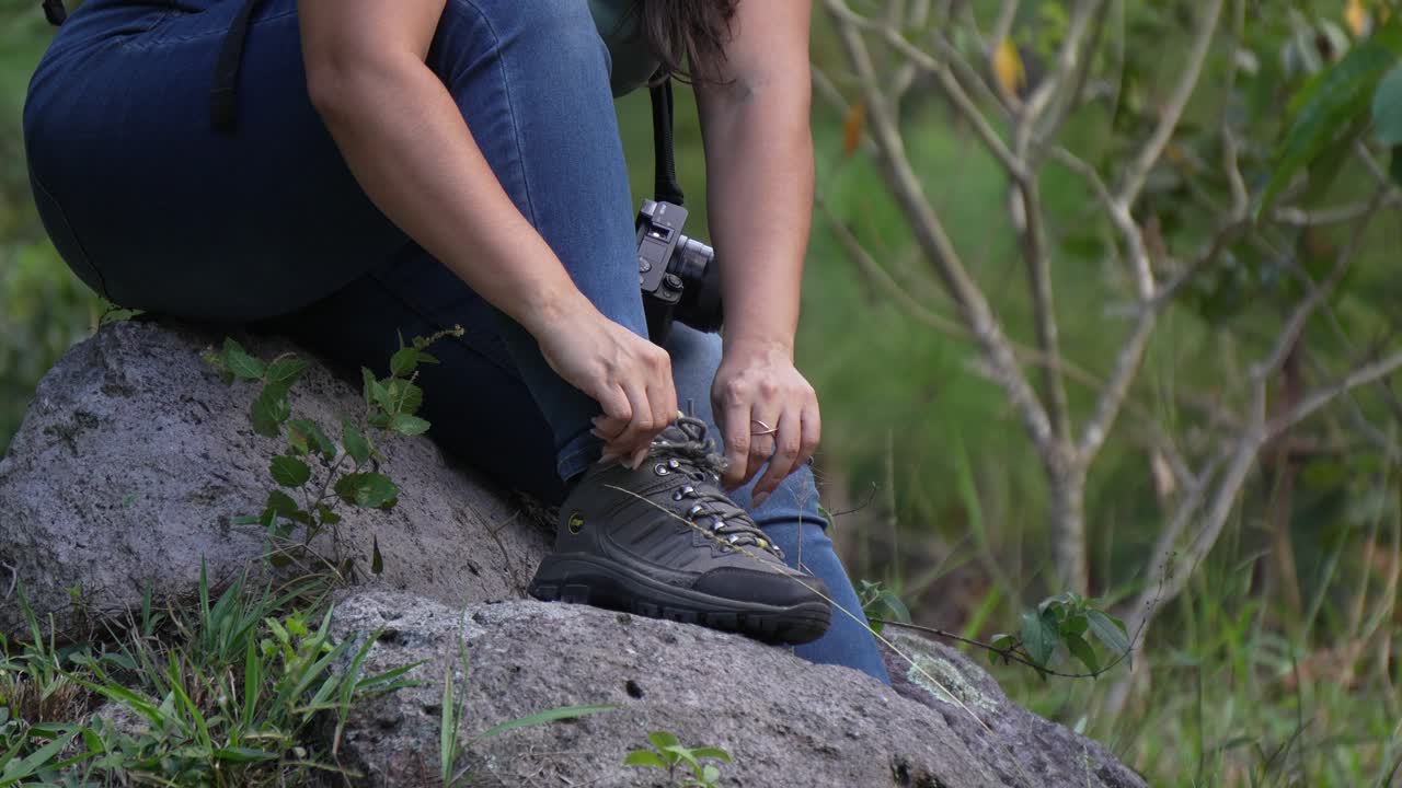 exploradora femenina con su mochila y cámara atando los cordones de sus zapatos mientras se prepara para una caminata en el bosque
