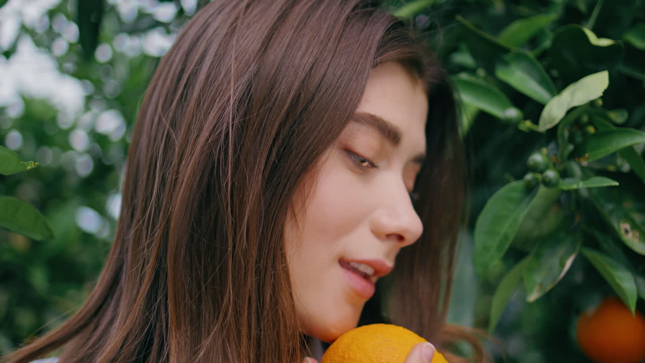 초록색 잎에 오렌지를 들고 있는 갈색 모델 초상화. 카메라를 찾는 여성