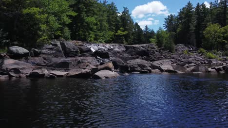 Low-drone-flyover-of-water-and-rocks-up-a-cascading-waterfall-in-Bracebridge,-Ontario