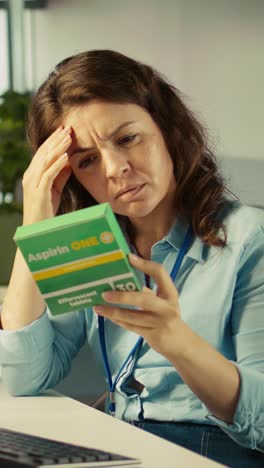 vertical video stressed woman in office feeling painful headache while working, taking pills