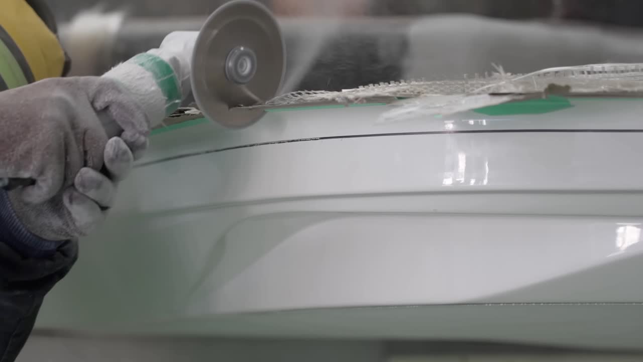 Close up of a craftsman using a pneumatic handheld cutting tool to trim the edges of a white fiberglass boat component