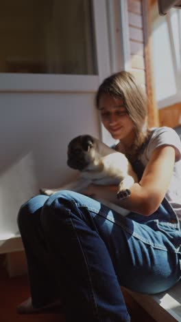 girl holding a pug dog by the window