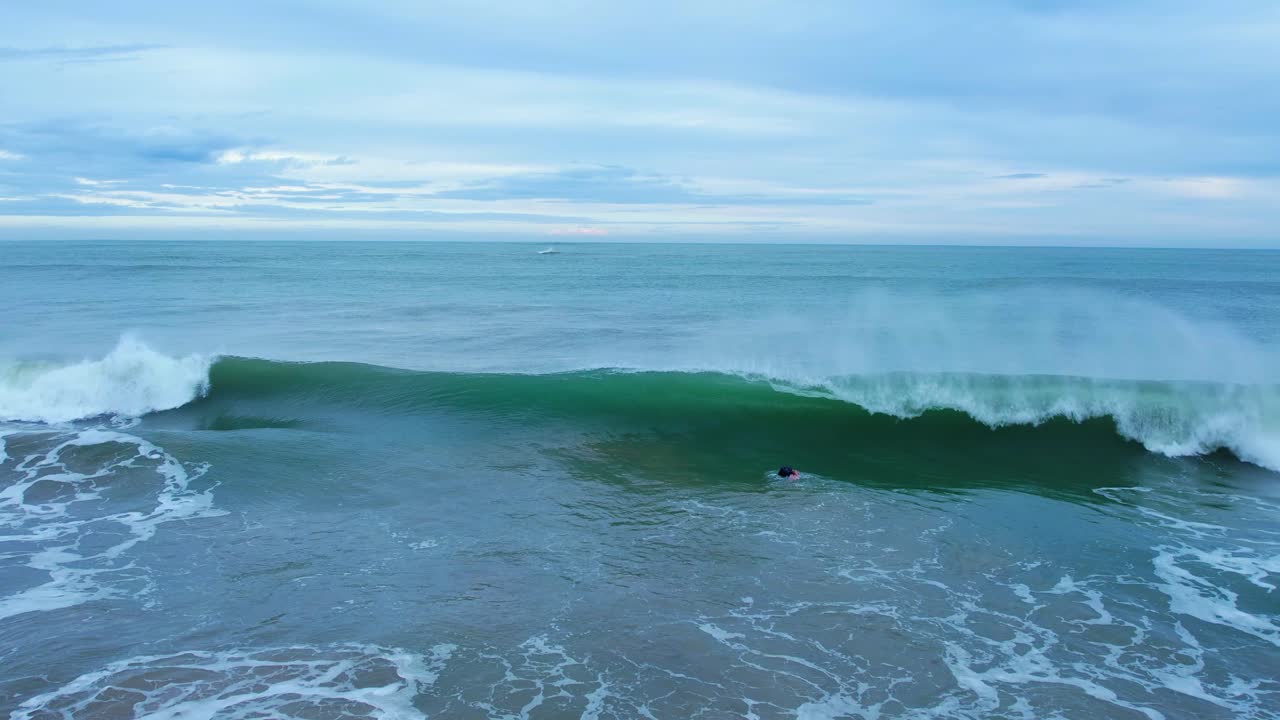 toma en cámara lenta de romper olas de surf y un surfista flotando en el mar azul