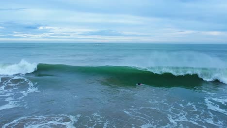 Slow-motion-shot-of-breaking-surf-waves-and-a-surfer-floating-in-the-blue-sea