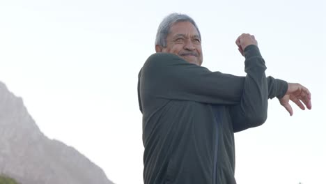 happy senior biracial man stretching and wearing sweatshirt in mountains