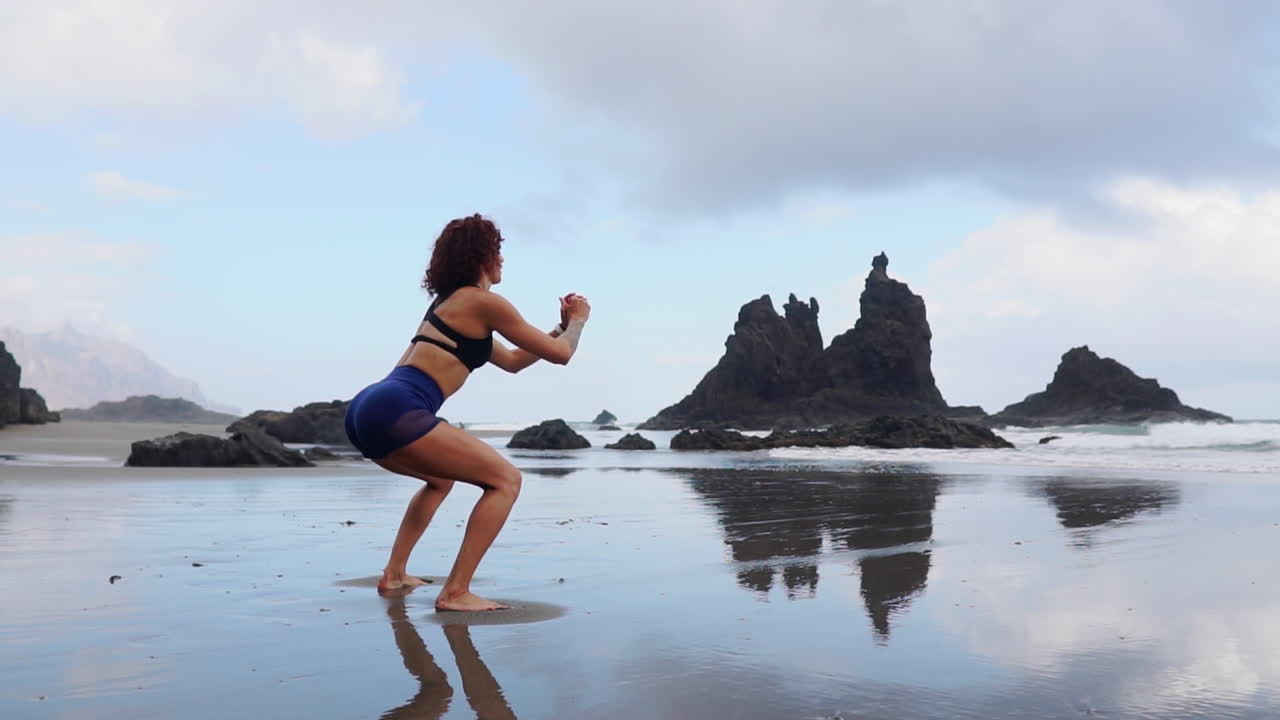 Fitness young woman working out core and glutes with bodyweight workout doing squat exercises on beach. Asian sporty girl squatting legs as part of an active and fit life