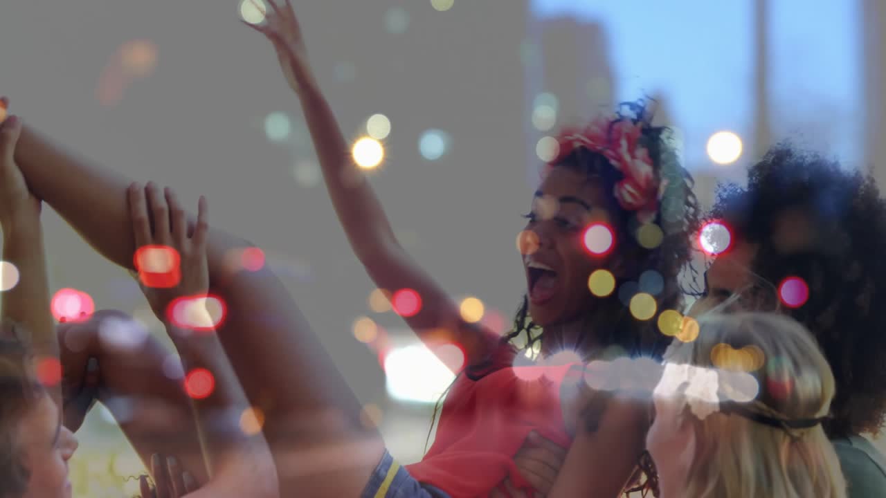 Amici che sollevano una donna sopra la testa a un festival, ridendo e agitando le braccia, con un overlay bokeh e dello skyline.