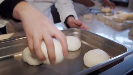 el chef forma los trozos de masa de pizza en la mesa de cocción y los coloca dentro de la bandeja de almacenamiento de metal