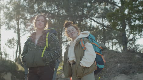 dos jóvenes mochileros mirando la cámara y sonriendo mientras caminan por el bosque en un día soleado