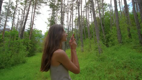 a woman on a hike in a green forest stops to examine and smell a fresh pinecone from the conifer trees above her