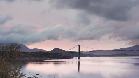 nubes tormentosas retroiluminadas de color rosa por la puesta se mueven sobre el fiordo y el puente