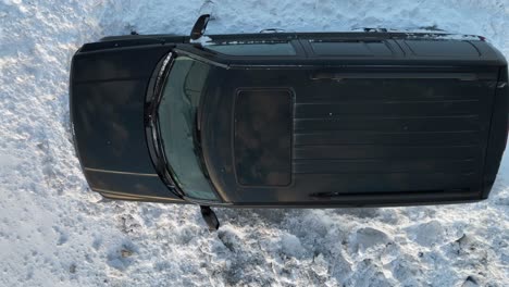 Top-down-aerial-of-black-vehicle-parked-in-white-winter-snow