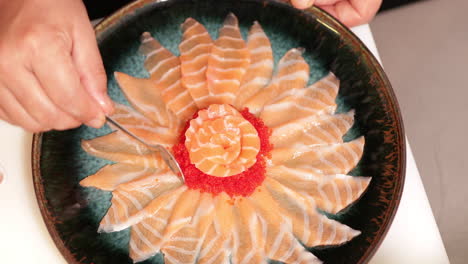 adding caviar to a plate of fresh salmon sashimi in floral arrangement using a teaspoon - overhead shot