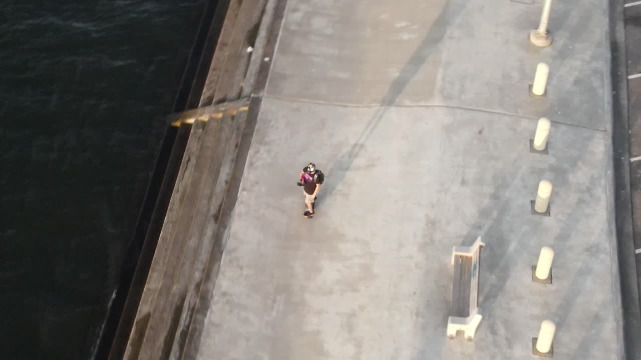 호숫가 공원의 에스플러네이드를 따라 달리는 전자 스케이트보드를 타는 배낭을 메고 있는 젊은이