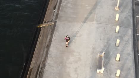 muchacho con mochila montando un monopatín electrónico corriendo a lo largo de la explanada en el parque a orillas del lago