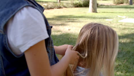 giovane figlia che intreccia i capelli della madre in un parco