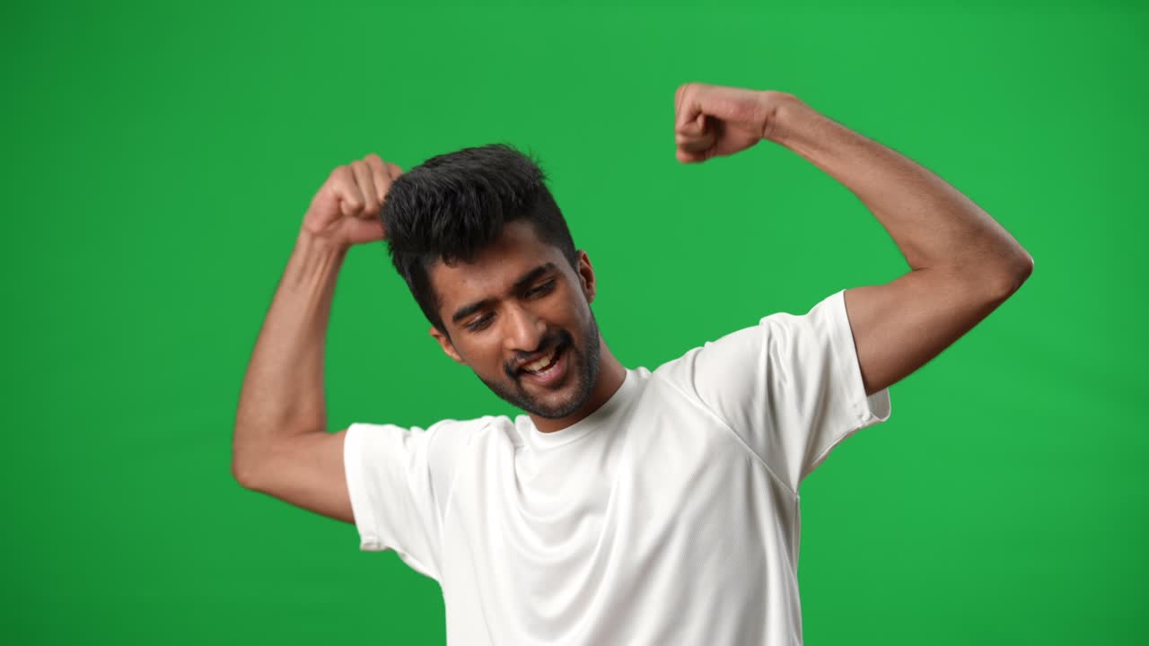 Excited handsome Middle Eastern football player gesturing victory posing on green screen. Portrait of satisfied successful young sportsman looking at camera smiling at chromakey background.