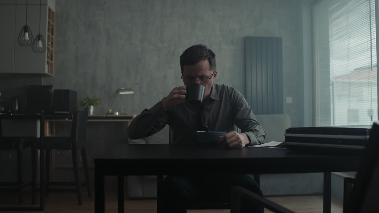 A sad man in a shirt slowly eats breakfast